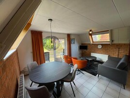 Una sala de estar moderna con una mesa de comedor, sillas color naranja, un sofá gris y un televisor montado en la pared.
