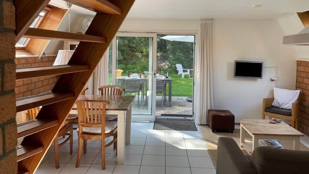 A modern living room with a staircase, a dining area, and a sliding glass door leading to an outdoor patio. - Holiday House in Friesland With Garden (Sint Nicolaasga)