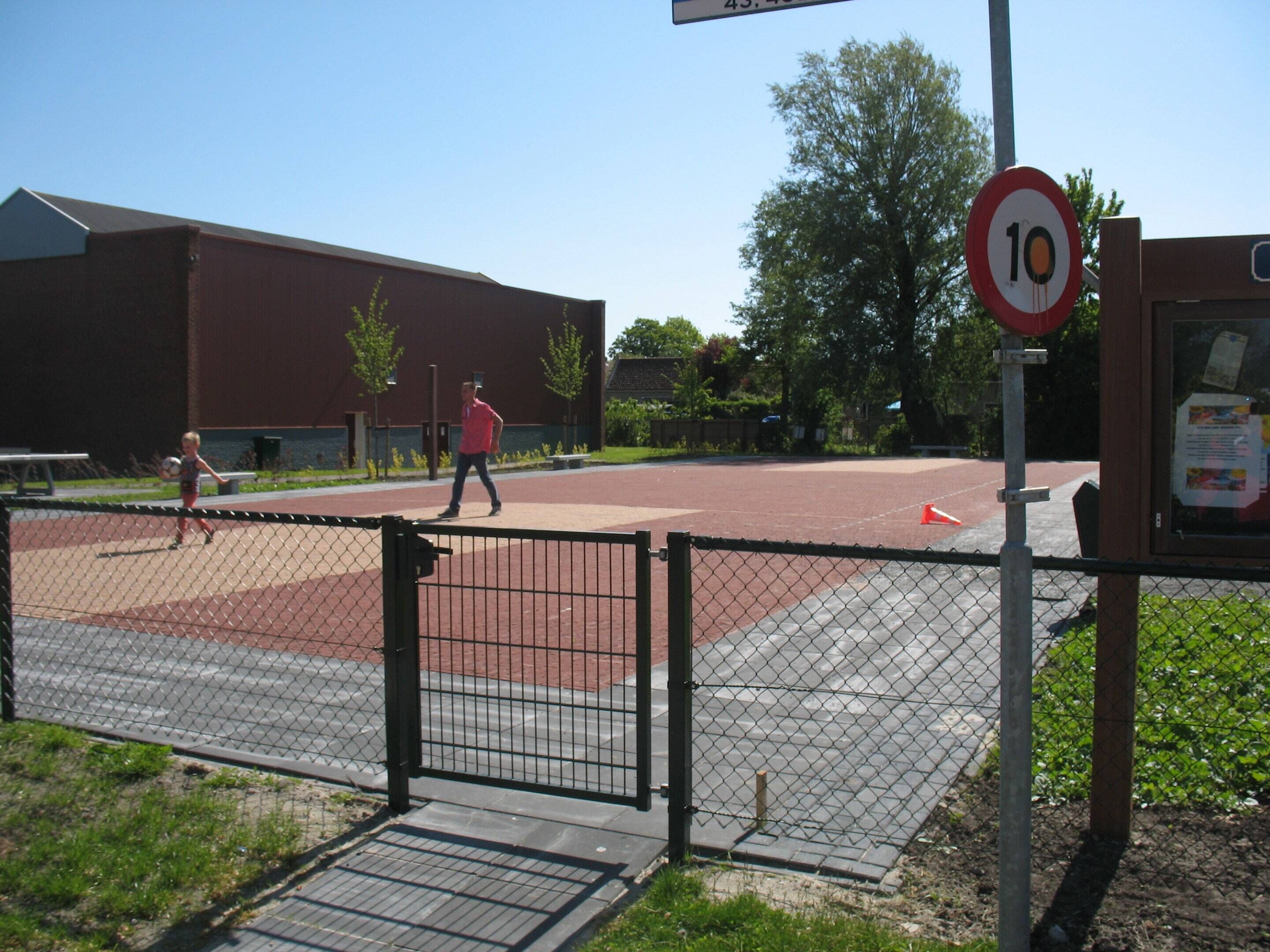A fenced sports court with a speed limit sign and a building in the background.