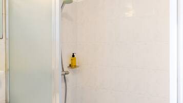 Baño con ducha acristalada, lavamanos blanco y una botella amarilla en un estante.