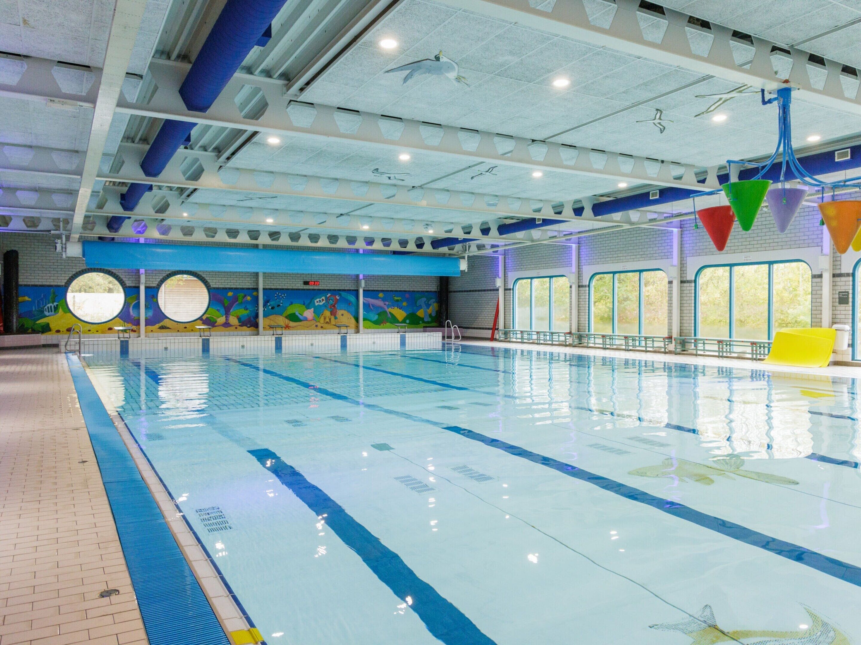 Une piscine intérieure avec des couloirs bien délimités, une fresque murale et un plafond orné de motifs géométriques.