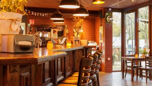 Una zona de bar con mostrador de madera, varias luces colgantes y un área de estar con sillas y mesas.