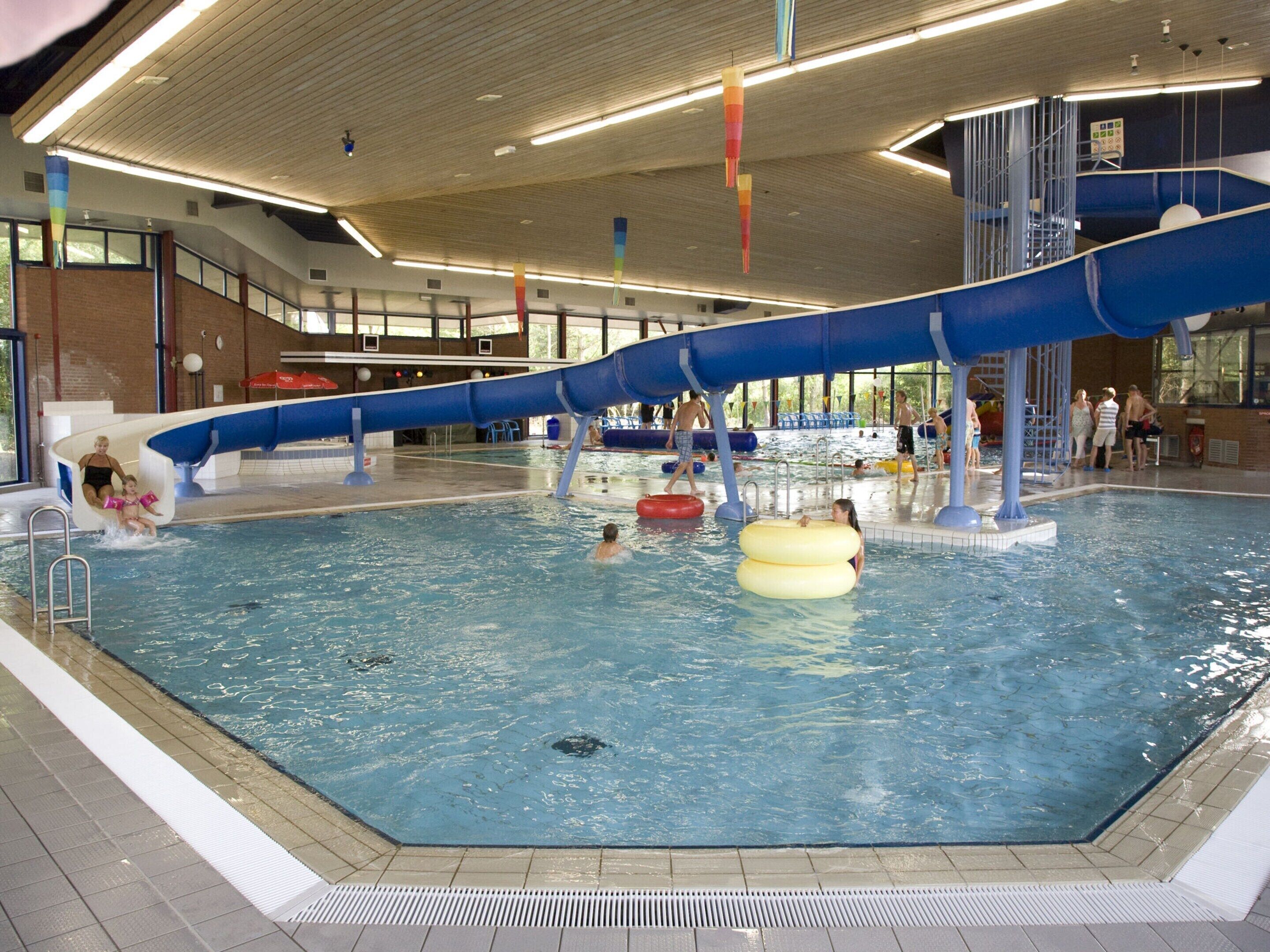 An indoor swimming pool with a blue water slide, multiple lanes, and a lifeguard stand.