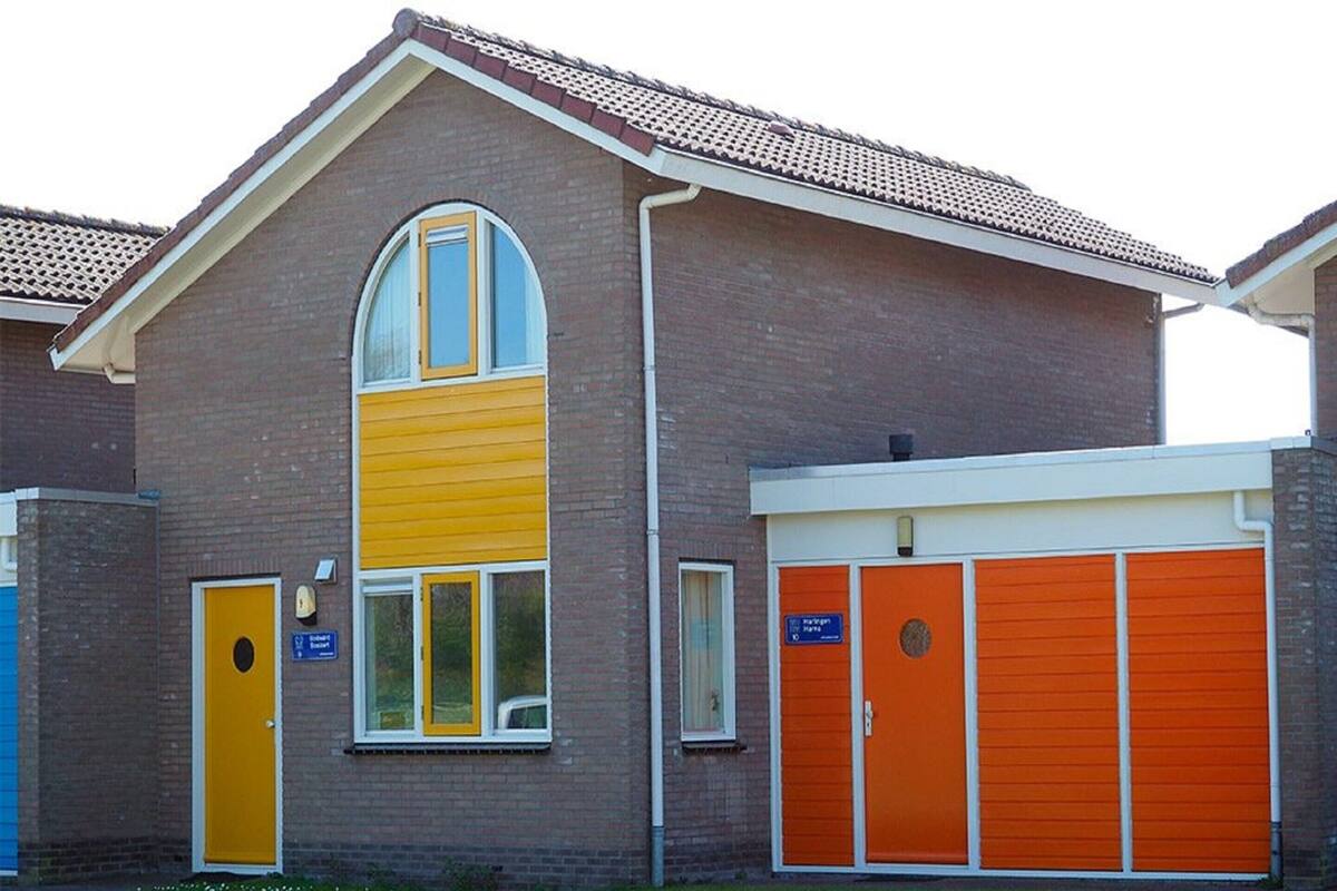 Un bâtiment à deux étages, doté d’une façade jaune et blanche, d’une grande fenêtre en arc de cercle et de portes de garage orange.
