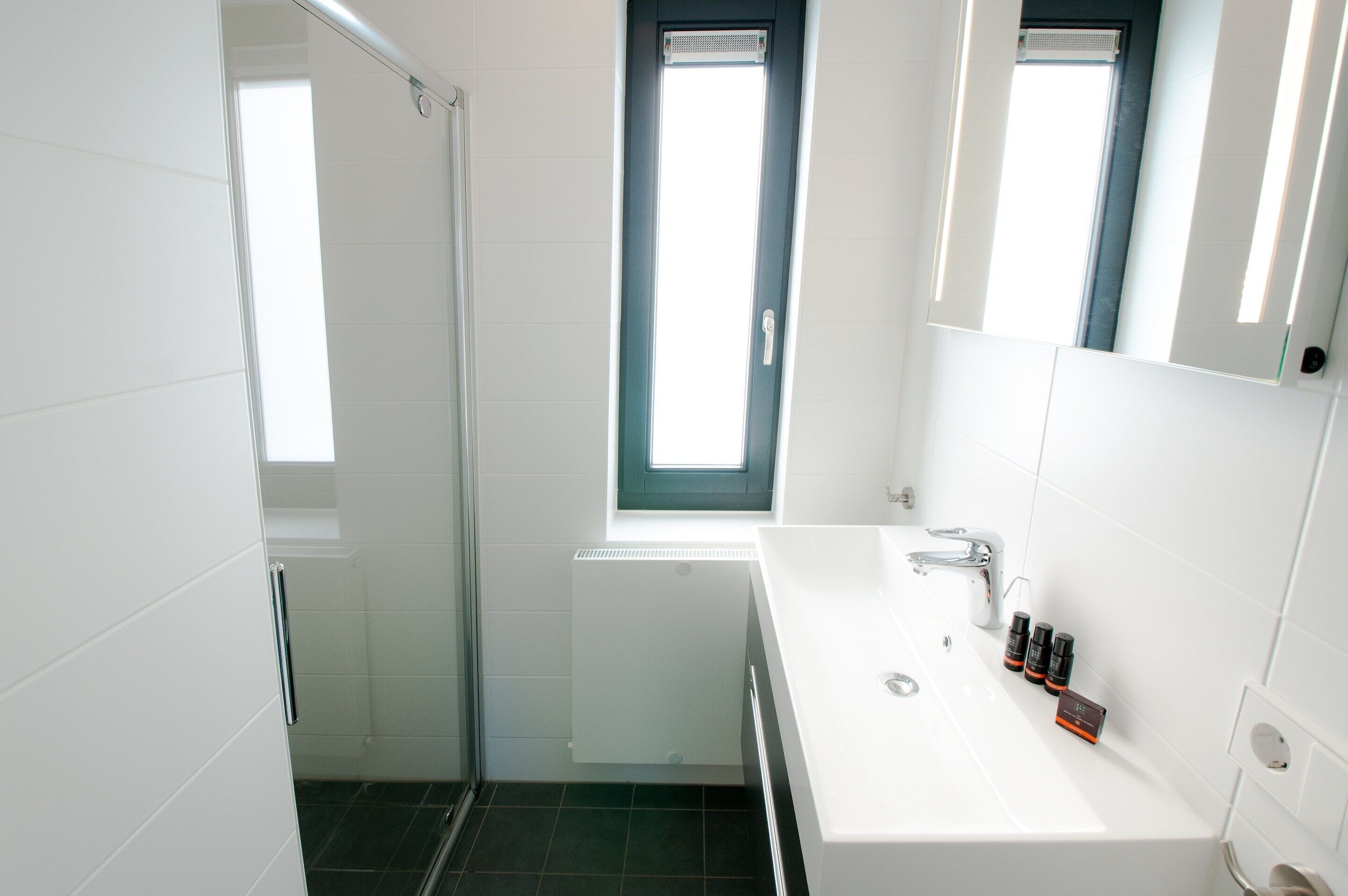 Een moderne badkamer met een douche, een wastafel en een raam.
