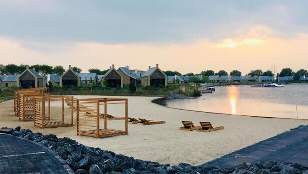 Un complexe hôtelier situé en bord de mer, avec des chalets en bois, une plage de sable et un lac paisible où l’on peut faire du bateau.