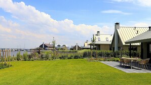 Une cour verdoyante avec une table et des chaises de patio, un plan d’eau et des bâtiments en arrière-plan.