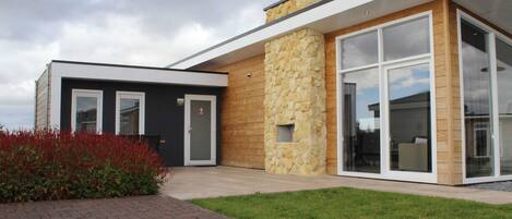 A modern house with a stone facade, large windows, and a brick pathway.