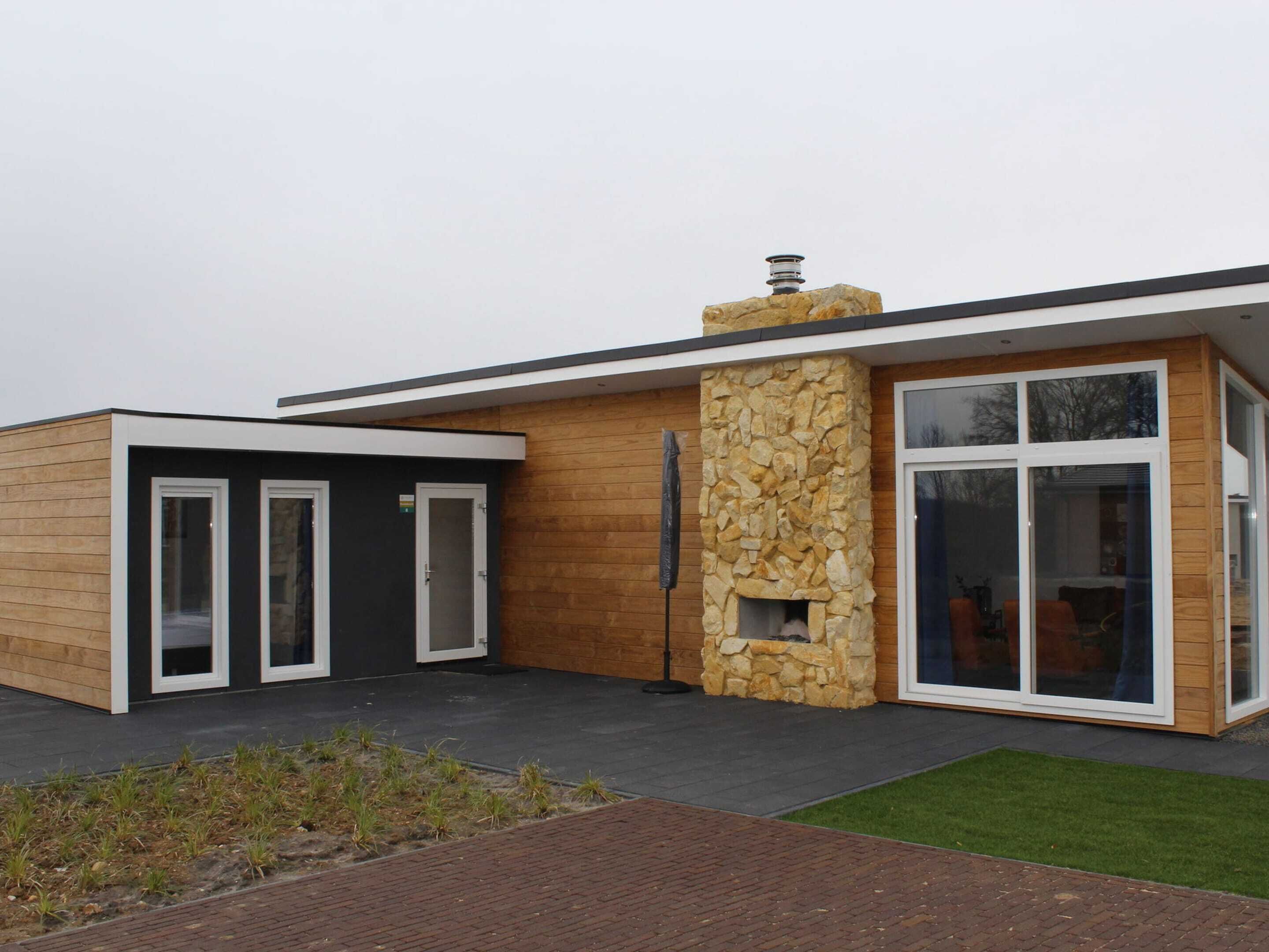 A modern house with a stone fireplace, large windows, and a wooden exterior.