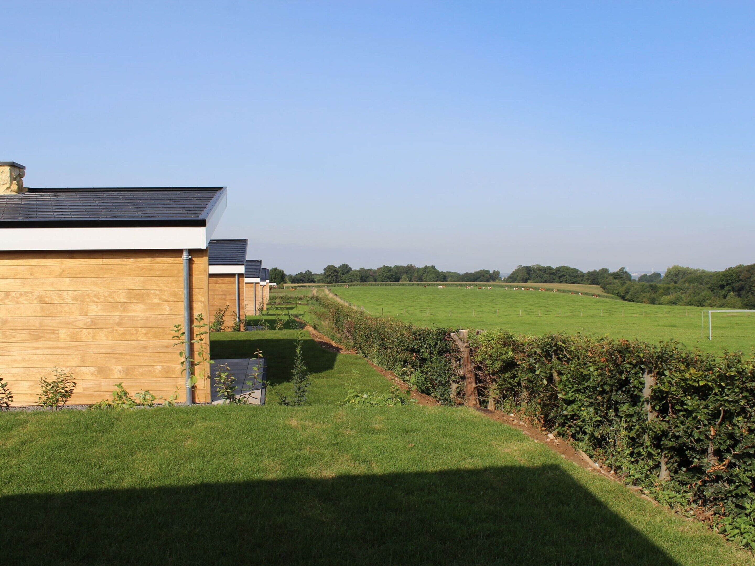 A modern building with a flat roof, adjacent to a well-maintained grassy field and a hedge.