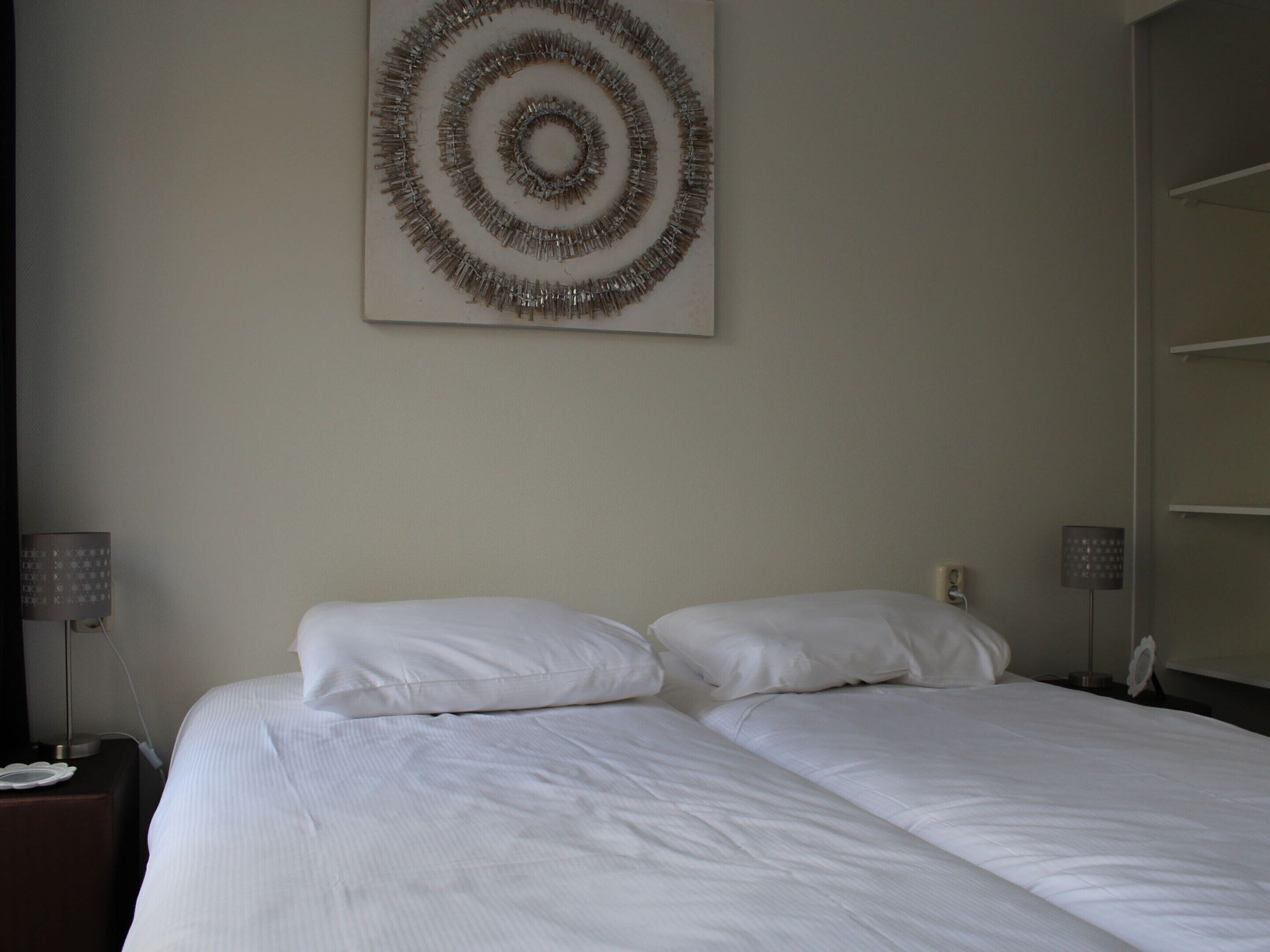 A hotel room with a large bed, two bedside tables, and a wall-mounted artwork.