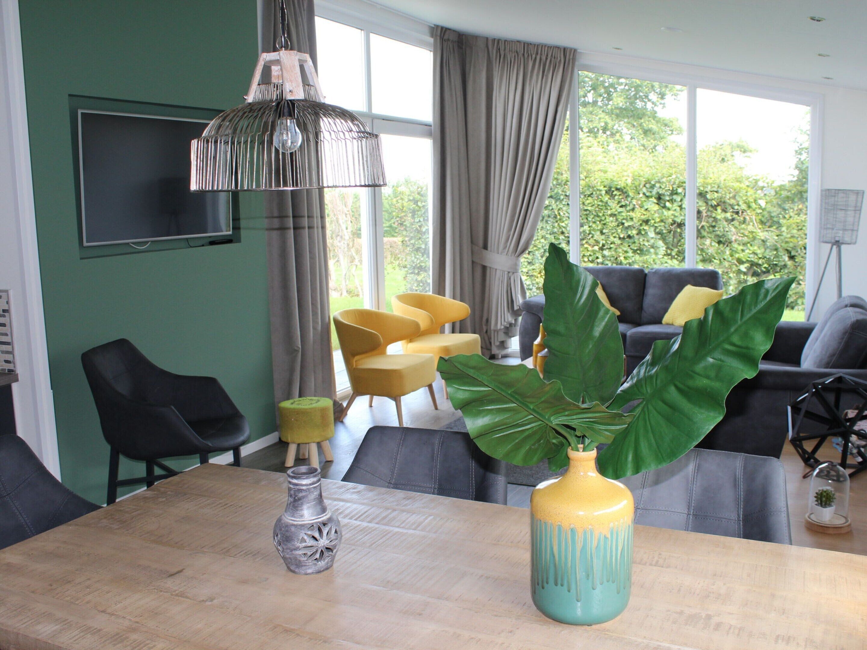 A dining area with a wooden table, a vase with a plant, and a hanging light fixture.