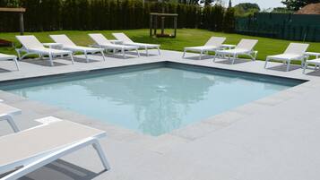 A rectangular swimming pool with white lounge chairs and tables arranged around it.