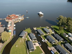 Luchtbeeld van een landgoed aan een meer, met meerdere steigers, een centraal gebouw met een rood dak en verschillende moderne huizen met aanhoudende garages.