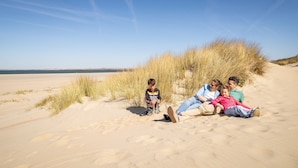Une famille de quatre personnes sur une plage de sable, avec des dunes et un ciel dégagé.