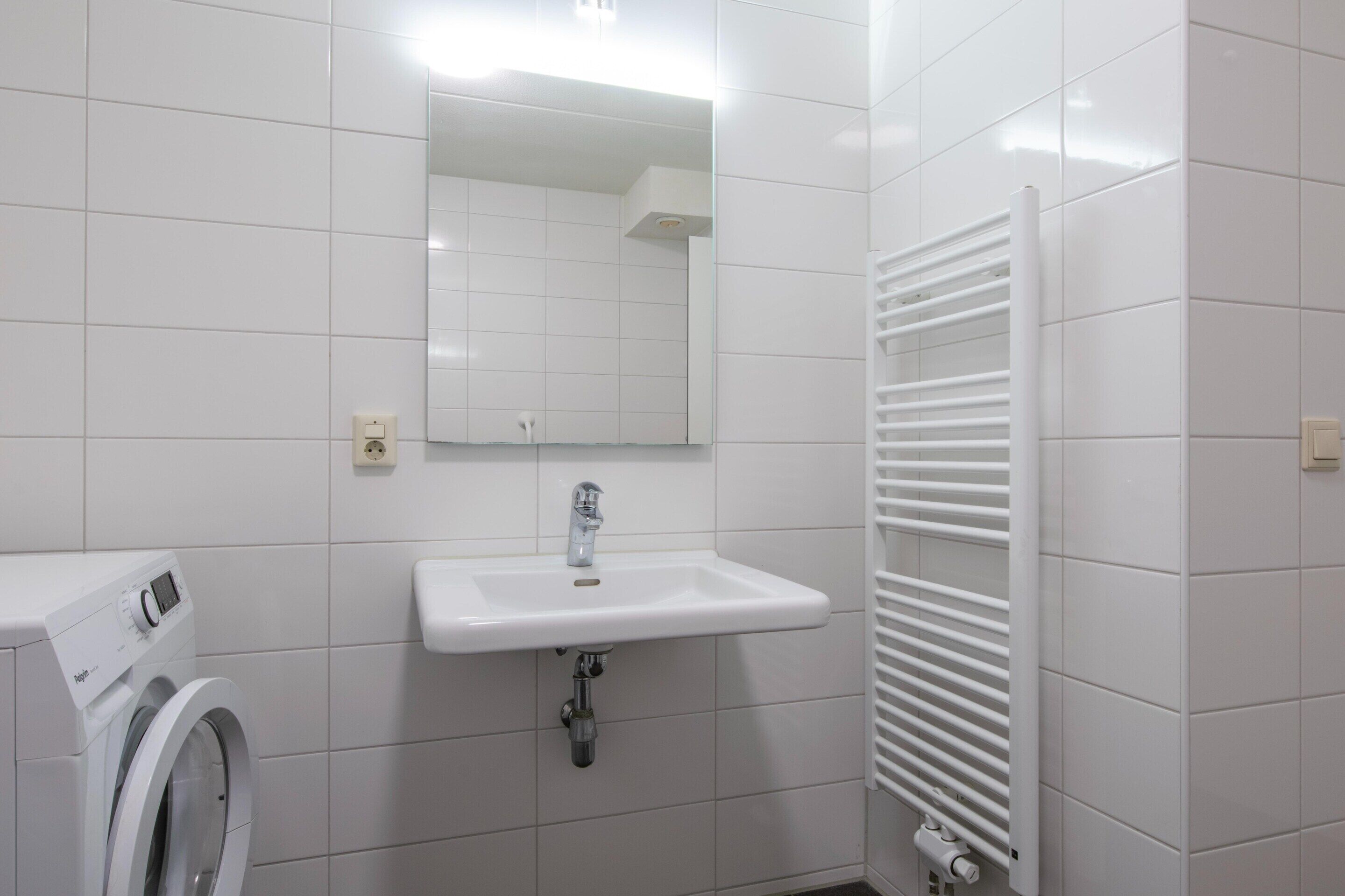 A bathroom with a white sink, a mirror, a towel rack, and a washing machine.