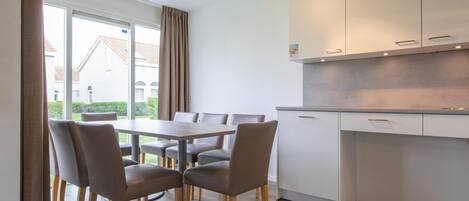A modern kitchen with white cabinets, a dining table with chairs, and a view of the outside.