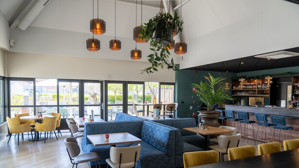 Un restaurant moderne doté d’un bar, d’un espace aménagé pour s’asseoir et de grandes fenêtres offrant une vue sur l’extérieur.