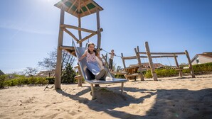 Une balançoire en bois avec un siège en métal et un auvent, située sur une plage de sable fin sous un ciel dégagé.