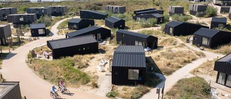 A coastal area with multiple modern, dark-colored cabins with flat roofs, arranged in a semi-circular pattern around a central path.