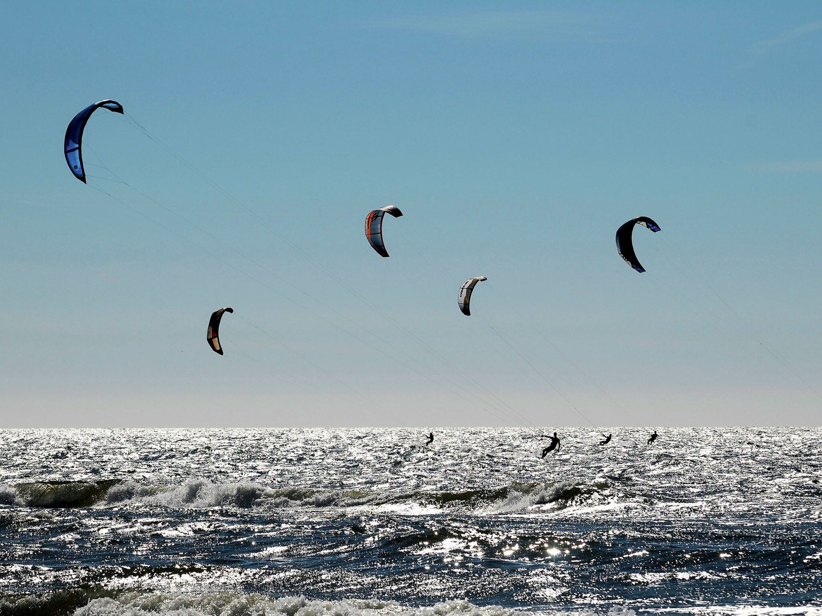 A beach with multiple kites flying in the sky and people surfing in the water.