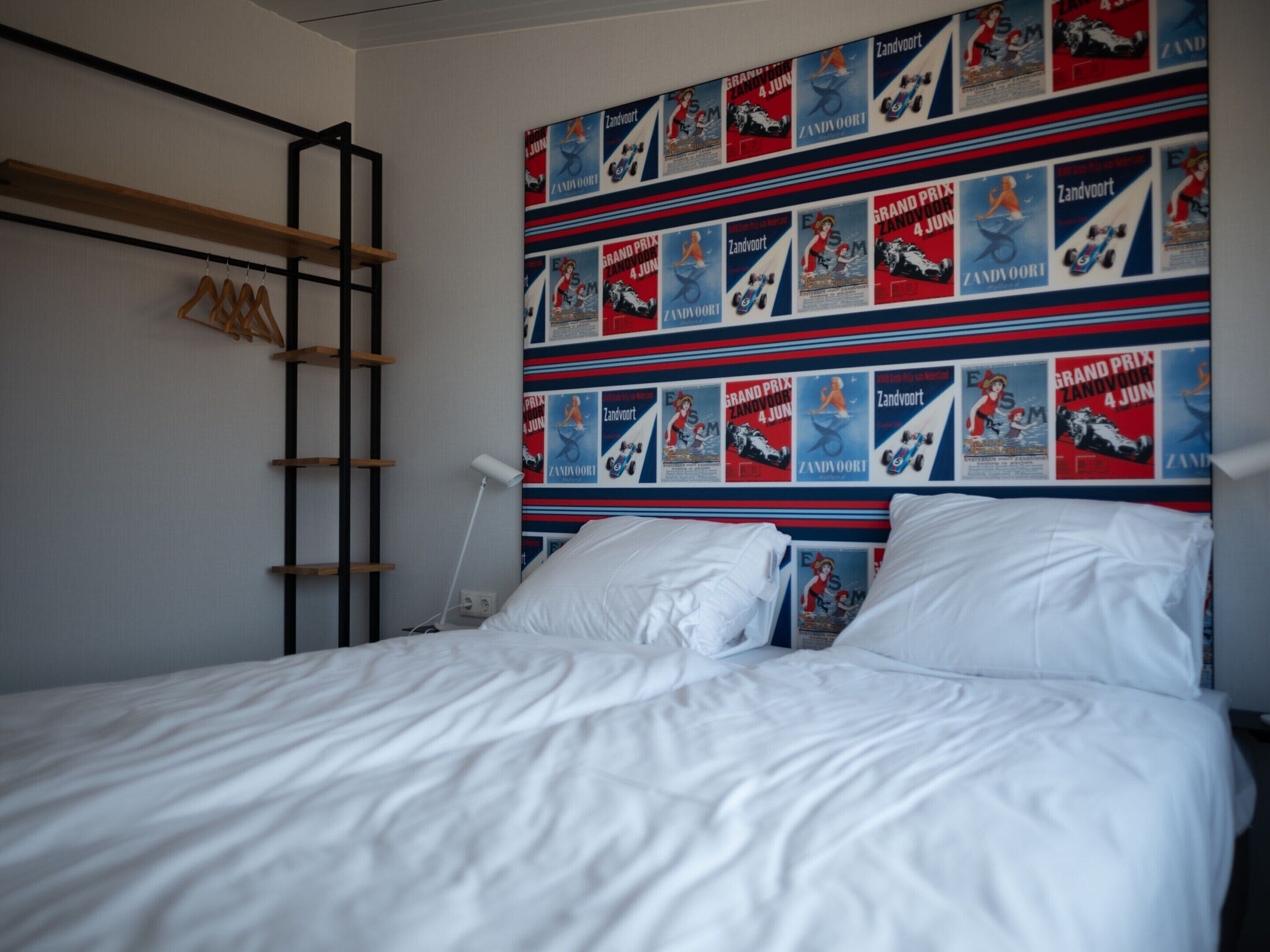 A bedroom with a bed, a wooden shelf, and a wall decorated with racing posters.