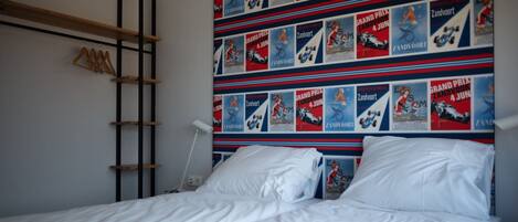 A bedroom with a bed, a wooden shelf, and a wall decorated with racing posters.
