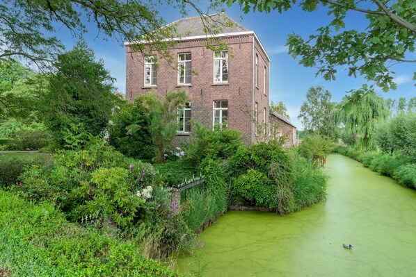 A brick building surrounded by lush greenery and a narrow water channel.