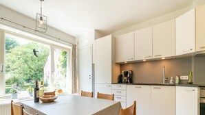 Ett modernt kök med vita skåp, ett matbord med en rutig duk och utsikt över grönskan utanför.