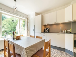 Een moderne keuken met witte kasten, een eettafel met geruit tafelkleed en uitzicht op groen buiten.