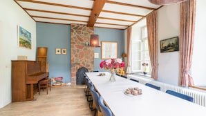 En matplats med ett långt bord, stolar, ett piano, en stenmur och ett fönster med gardiner.