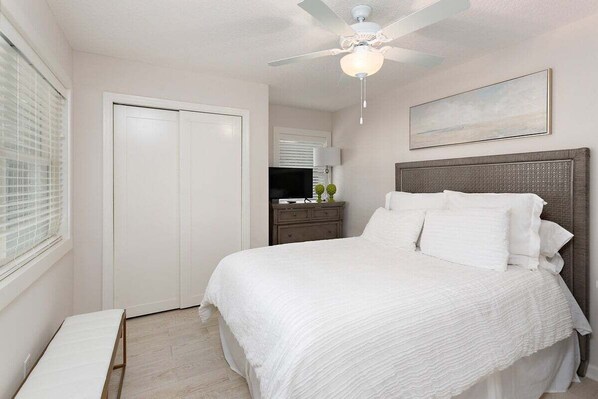A bedroom with a bed, a ceiling fan, a nightstand, a TV, and a window with blinds. - Pet Friendly with private pool and fenced yard! (Saint Simons Island)