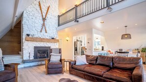 A spacious living area with a stone fireplace, leather sofas, and a high ceiling with a balcony. - Lakefront, beach, hot tub, putt course, paddleboards, boat ramp, deck, fireplace (East Wenatchee)