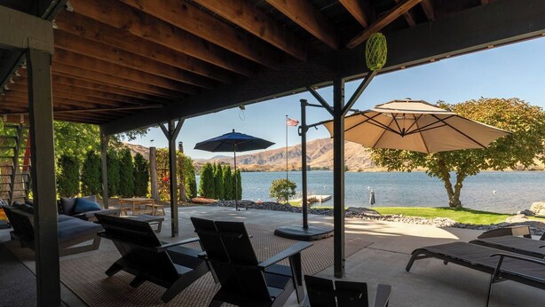 A covered patio with outdoor seating, a view of a lake, and a flag. - Lakefront, beach, hot tub, putt course, paddleboards, boat ramp, deck, fireplace (East Wenatchee)