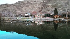 A lakeside property with multiple buildings, a dock, and a reflection in the water. - Lakefront, beach, hot tub, putt course, paddleboards, boat ramp, deck, fireplace (East Wenatchee)