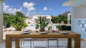 A wooden dining table set with plates, glasses, and a potted plant, overlooking a swimming pool and lush greenery. - 🌴 5 Bed Villa, Ocean View , Pool with Jacuzzi, Near Crane beach🌴 (Saint Philip)