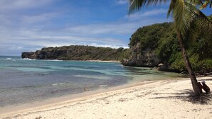 A beach with clear turquoise water, sandy shore, and a rocky cliff with vegetation. - NEW! Luxury villa with private pool (sainte anne)