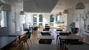 A spacious dining area with multiple tables and chairs, large windows, and a view of the outdoors. - Auberge de Jeunesse Orléans Centre Ville - Hostel (Orléans)