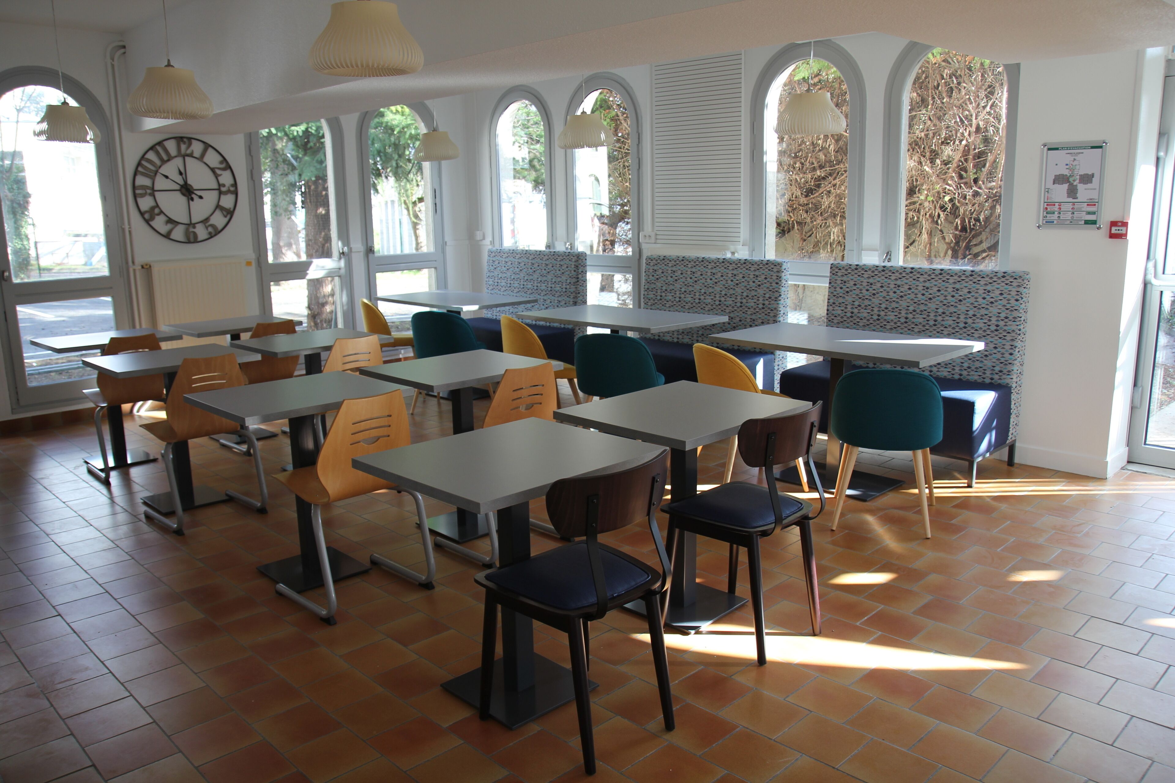 Un restaurante con varias mesas y sillas, amplias ventanas y un reloj en la pared.