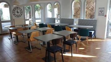 Un restaurante con varias mesas y sillas, amplias ventanas y un reloj en la pared.