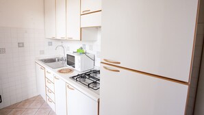 A kitchen with white cabinets, a gas stove, a microwave, and a sink. - APP.TI VILLA ANNA - VILLA ANNA - TRILO PRIMO PIANO (Capoliveri)