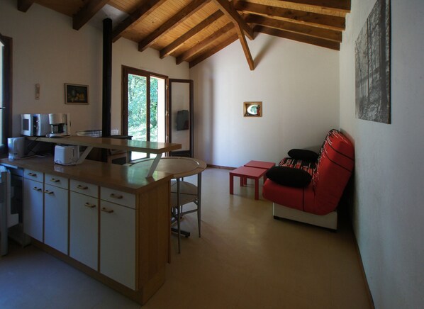 Una cocina con techo de madera, una zona de comedor con una silla roja y una mesa pequeña.