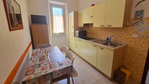 A compact kitchen with yellow cabinets, a tiled backsplash, a sink, and a window with curtains. - SOLILUNA on the seafront of Cavo (Rio Marina)