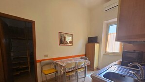 A compact kitchen with a sink, a small table, and chairs. There is a television on a cabinet, and a window with curtains. - SOLILUNA on the seafront of Cavo (Rio Marina)
