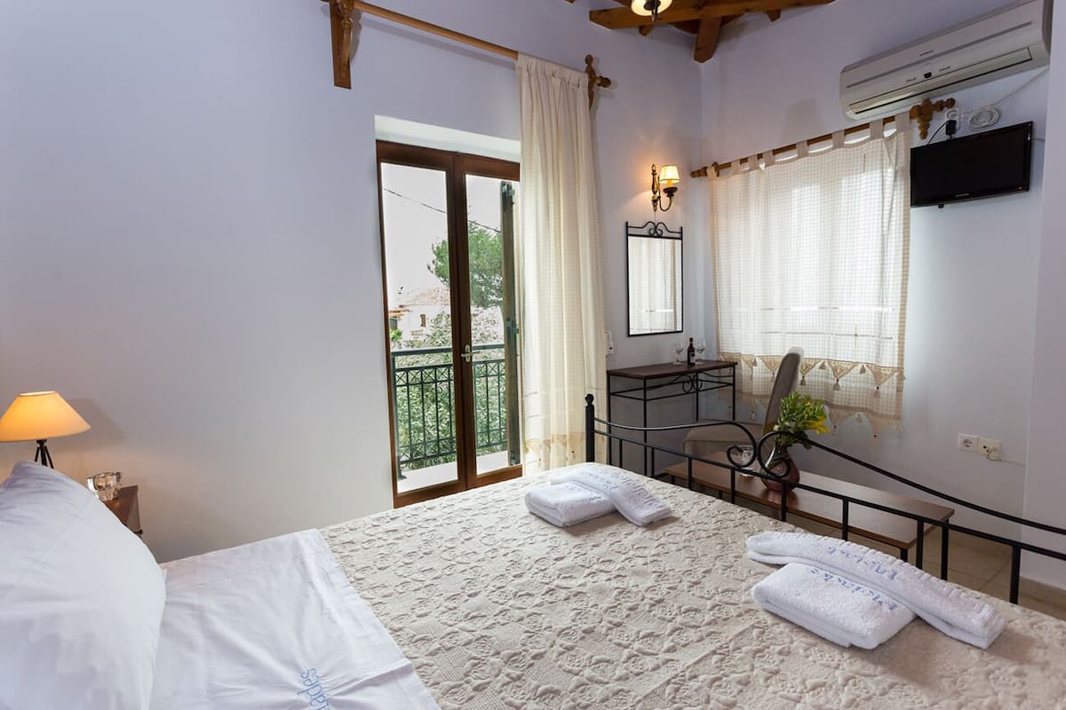 A bedroom with a bed, a nightstand, a lamp, a window with curtains, a mirror, a desk, and a chair.