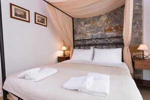 Una cama bien hecha con sábanas y toallas blancas, un muro de piedra detrás del cabecero y dos cuadros en la pared.
