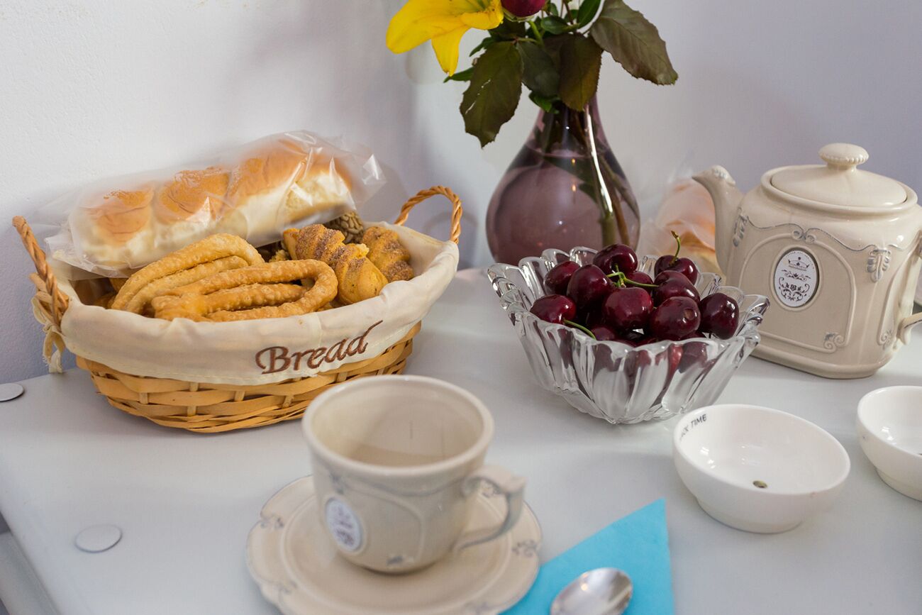 Ein Tisch mit einem Brotkorb, einer Schale Kirschen, einem Teekännchen und einer Tasse.