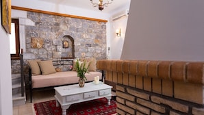 Una sala de estar acogedora con una pared de piedra, un sofá, una mesa de centro blanca y una alfombra roja estampada.