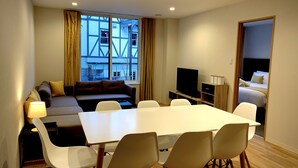 Une chambre d’hôtel moderne dotée d’une grande fenêtre, d’un canapé, d’une télévision, d’une table à manger avec des chaises et d’un espace chambre séparé.