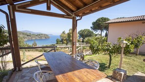 A wooden table and chairs under a pergola with a view of the sea and hills. - RESIDENZA IL GABBIANO - VILLINO GABBIANELLA (Capoliveri)